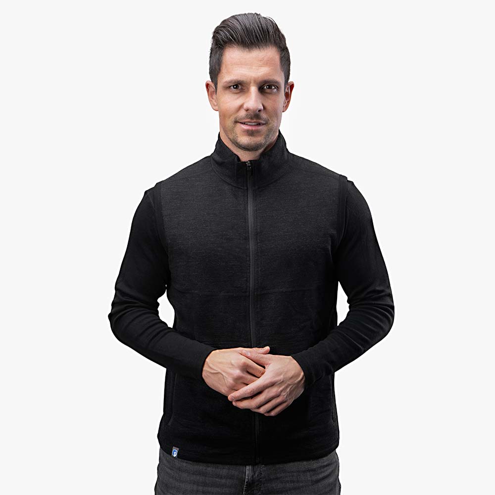 Mann trägt Merino Weste Herren 270 g/m², eine stilvolle, funktionale Wollweste mit Reißverschluss und Seitentaschen, ideal als Midlayer für Outdoor-Aktivitäten.
