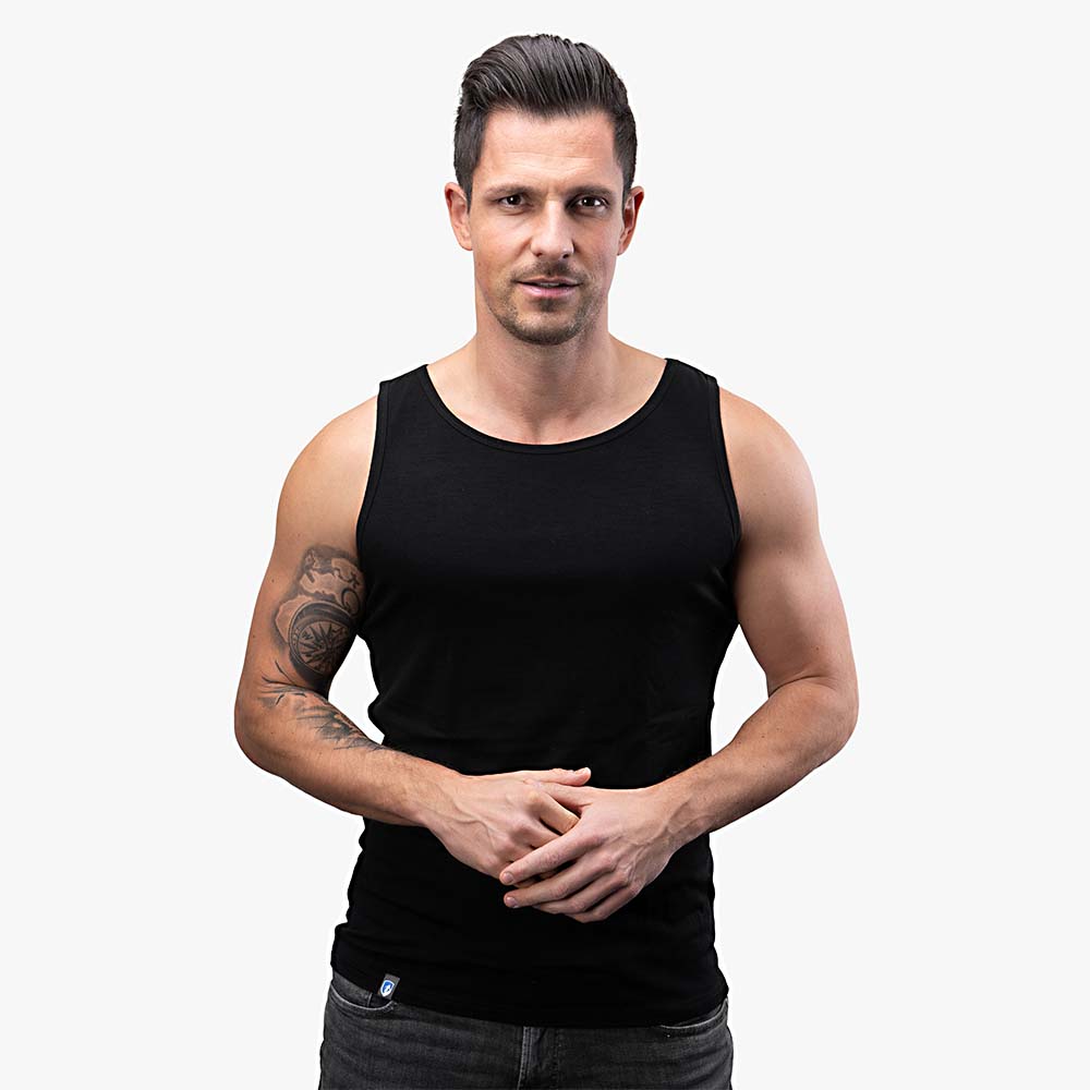 Mann trägt das Merino Tank Top Herren 150 g/m2, ideal für Outdoor-Aktivitäten, zeigt Muskeln und Kompass-Tattoo auf dem Arm. Perfekt für Sport und Reisen.