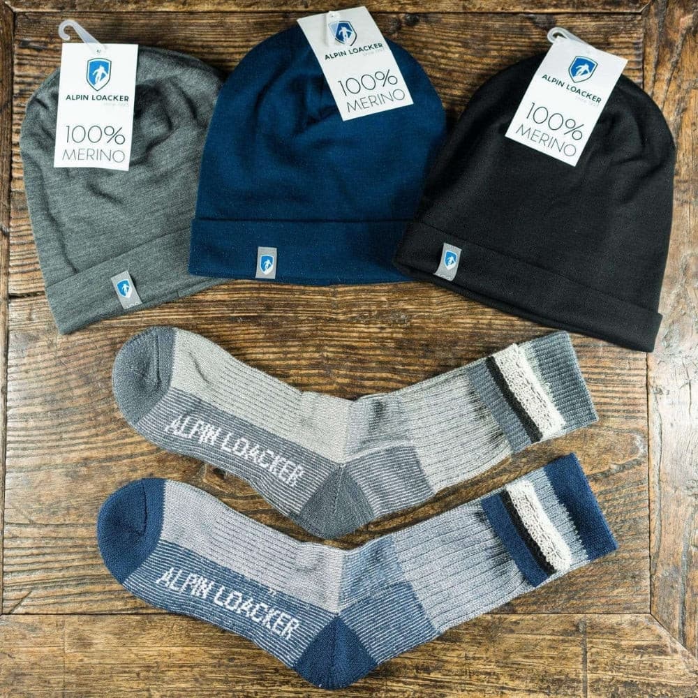 Merino Wandersocken Classic Herren & Damen und drei Merino-Mützen von Alpin Loacker auf rustikalem Holz, betont Komfort und Langlebigkeit für Outdoor-Aktivitäten.