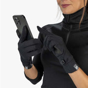 Person mit schwarzen Merino Handschuhe mit Touch Funktion bedient ein Smartphone. Die Handschuhe sind robust, atmungsaktiv und ideal für Outdoor-Aktivitäten im Winter.