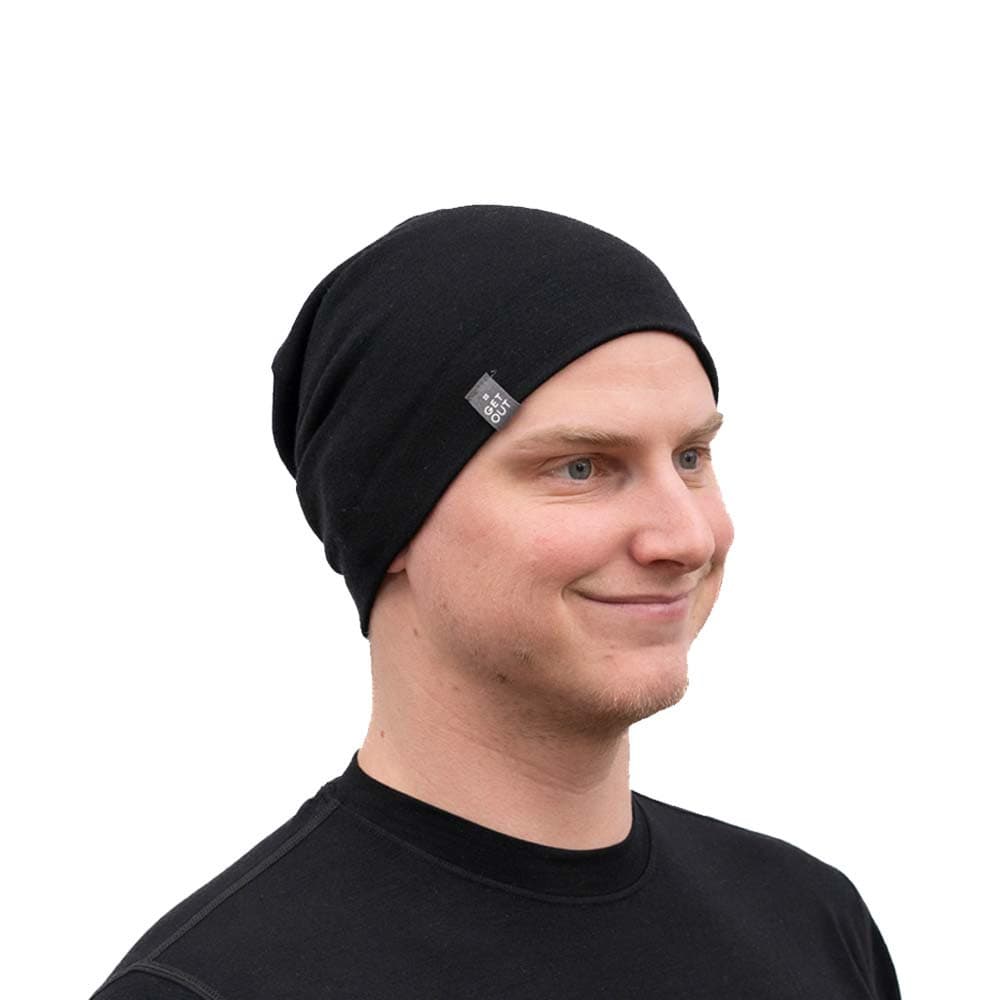 Person trägt eine Merino Mütze Herren & Damen 230g/m², schwarzer Strick, aus 100% Merinowolle, ideal für Outdoor-Aktivitäten, leicht und komfortabel, dezentes Lächeln.