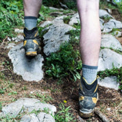Person auf Waldweg trägt Merino Wandersocken Classic Herren & Damen, kombiniert mit robusten Wanderschuhen, um unebenes Gelände zu meistern. Ideal für Outdoor-Abenteuer.
