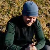 Mann trägt Merino Weste Herren 270 g/m², lacht sitzend im Freien. Perfekt für Outdoor-Touren und Freizeit, bietet Komfort und Stil.
