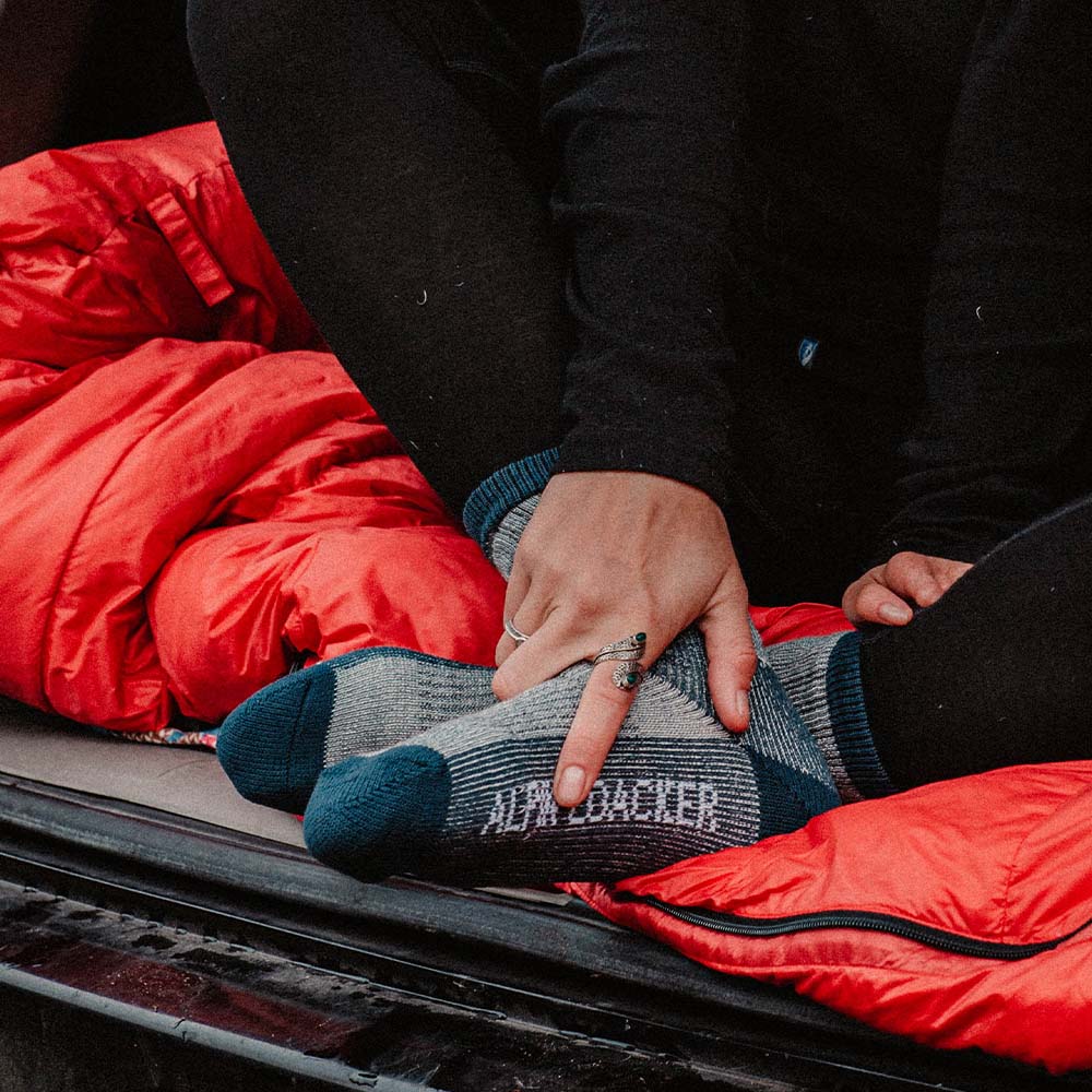 Merino Wandersocken Classic Herren & Damen: Nahaufnahme von Füßen in grauen Socken, Finger zeigt auf Schriftzug. Perfekt für Outdoor-Abenteuer, aus 72% Merinowolle gefertigt.