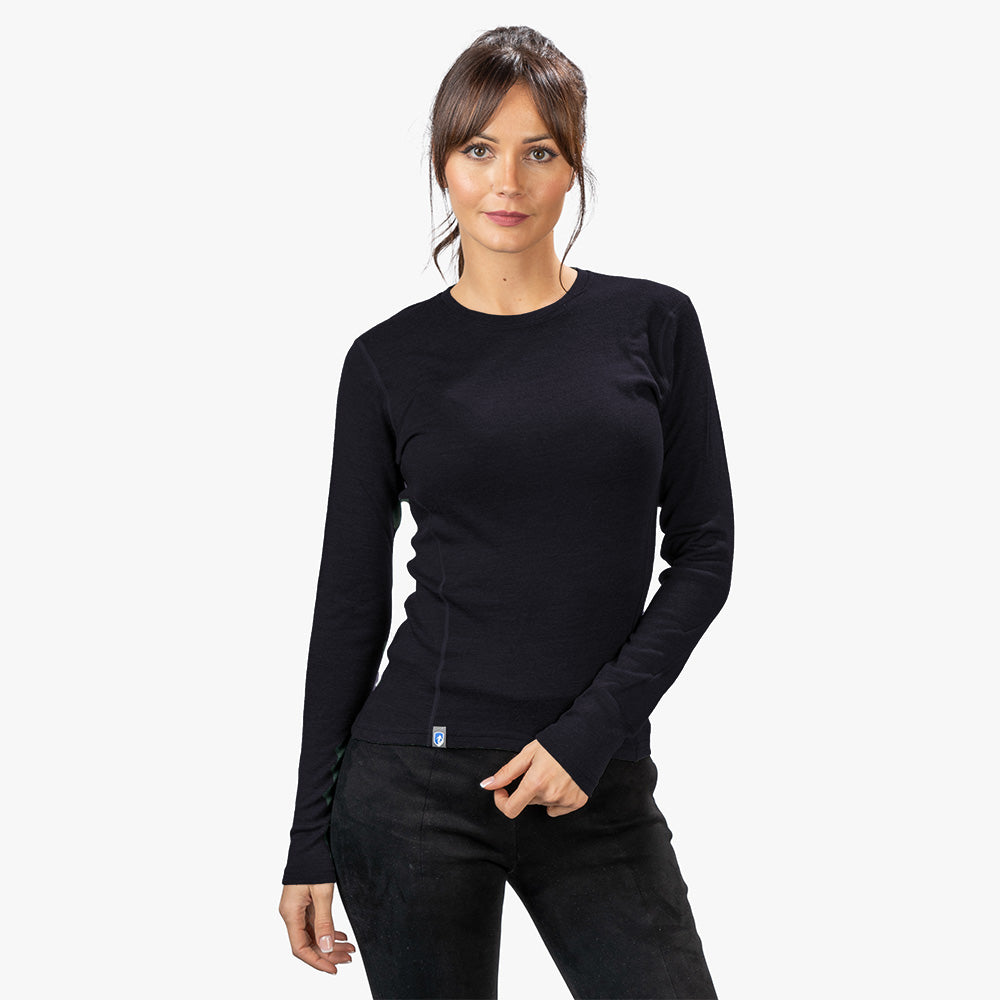 Frau in Alpin Loacker Merino Langarmshirt für Damen aus 100% Merinowolle, ideal für Outdoor-Aktivitäten, steht vor hellem Hintergrund.