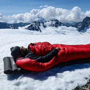 Person ruht in rotem Schlafsack auf der Leichte Isomatte isoliert mit Kunstdaune, auf schneebedecktem Gebirgskamm. Perfekt für alpines Camping und Trekking.