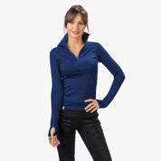 Frau trägt Merino Langarmshirt mit Zip Damen 230g/m2, ausgestattet mit Daumenlöchern, ideal für Outdoor-Aktivitäten. Kombiniert mit schwarzen Slim-Fit-Hosen.