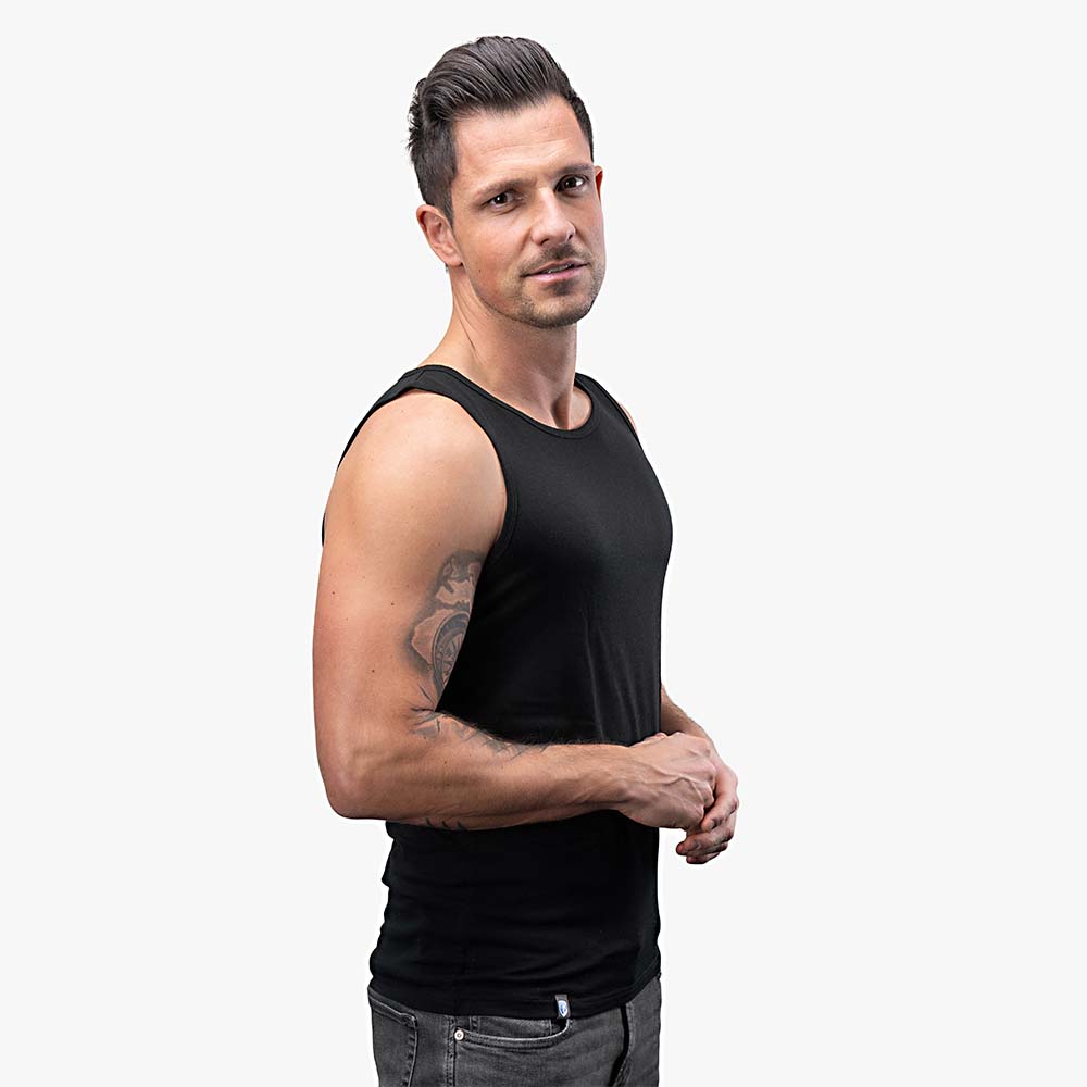 Mann trägt Merino Tank Top Herren 150 g/m2, zeigt Tattoo am Arm, ideal für Outdoor-Aktivitäten mit Komfort und Langlebigkeit durch CORESPUN-Technologie.