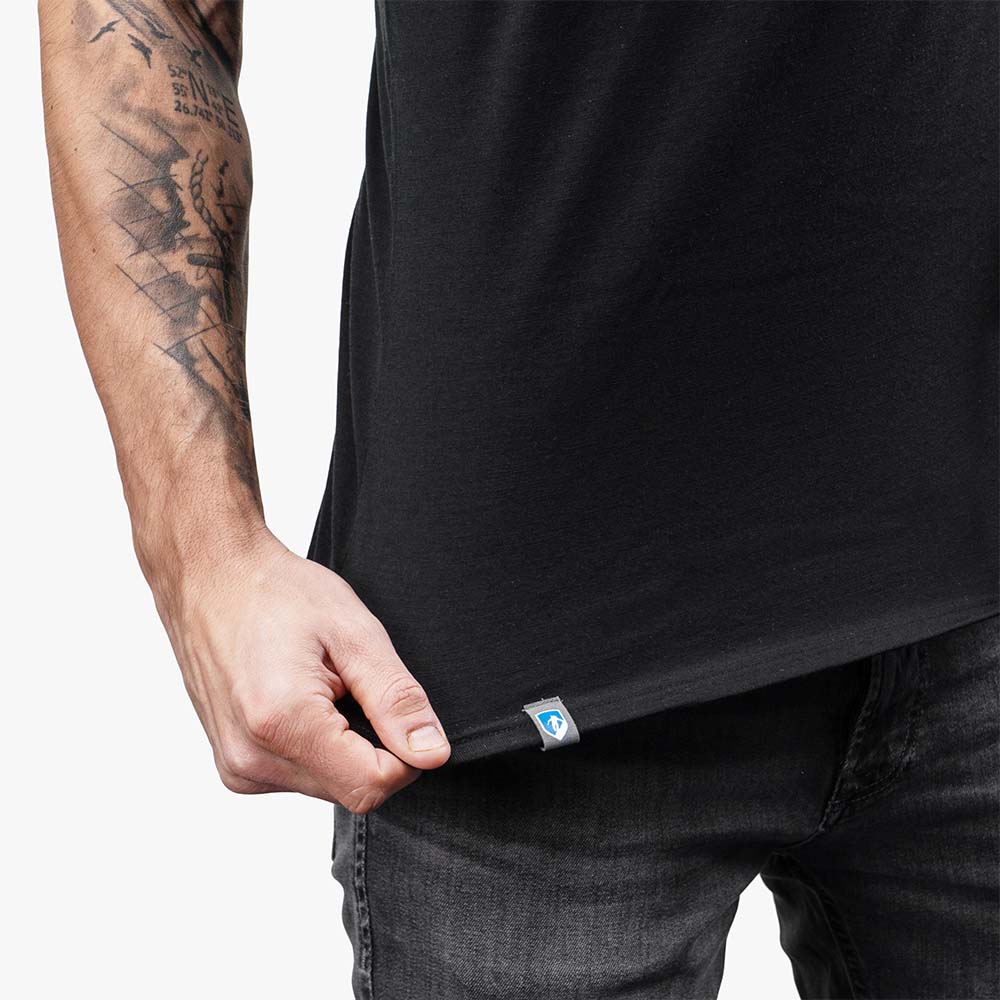 Mann zeigt das Merino Tank Top Herren 150 g/m2 mit sichtbarem gewebtem Etikett; ideal für Outdoor-Aktivitäten dank CORESPUN-Technologie und Merinowolle.