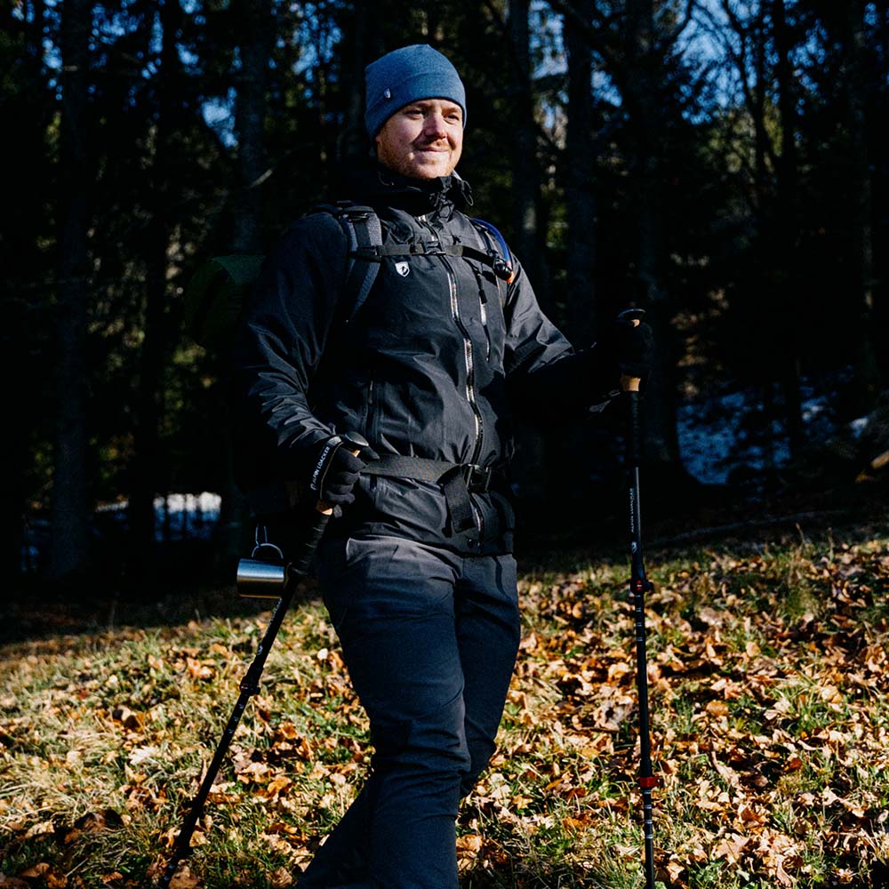 Mann auf Waldweg mit Merino Handschuhe mit Touch Funktion, ideal für Outdoor-Aktivitäten. Trägt Trekkingstöcke und Rucksack, passend für Herbst- oder Winterwanderungen.