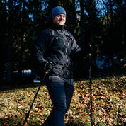 Mann auf Waldweg mit Merino Handschuhe mit Touch Funktion, ideal für Outdoor-Aktivitäten. Trägt Trekkingstöcke und Rucksack, passend für Herbst- oder Winterwanderungen.