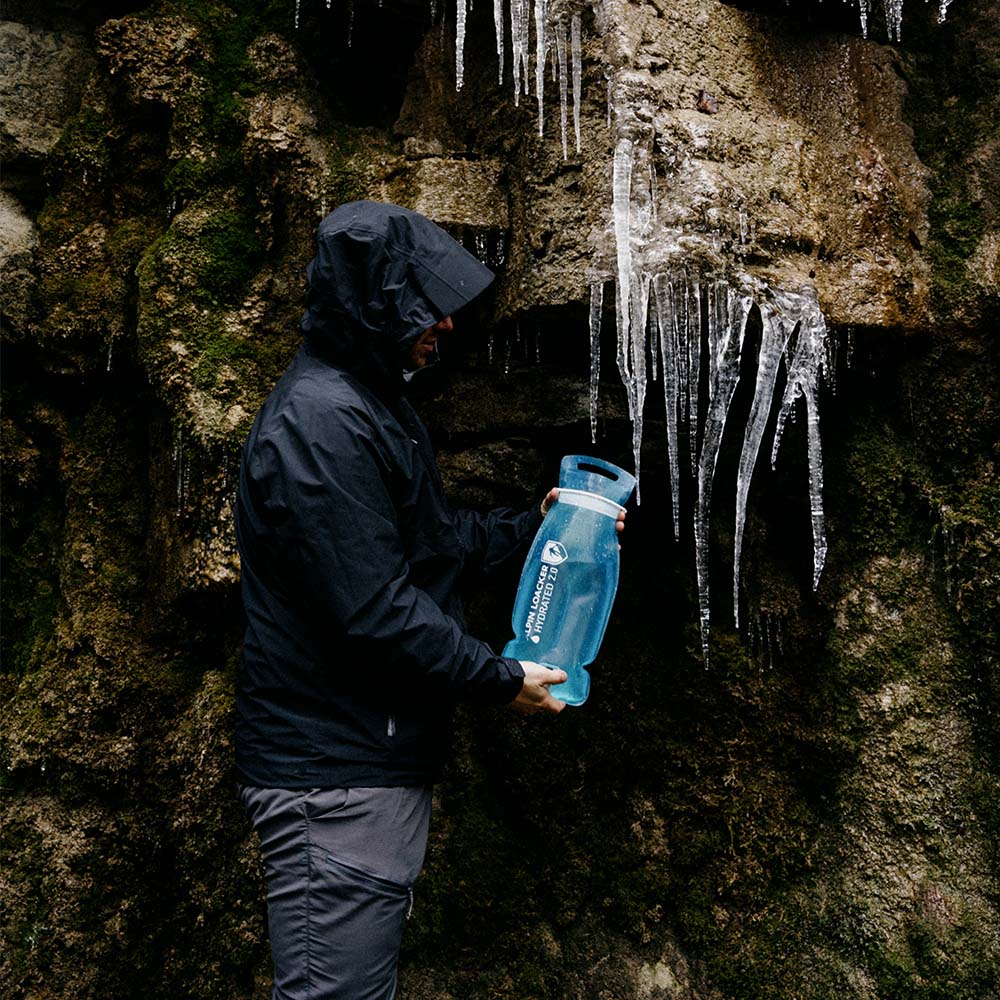 Person füllt die Alpin Loacker Trinkblase für Sommer + Winter mit Schmelzwasser aus eisbedecktem Felsen, ideal für Outdoor-Aktivitäten wie Wandern und Trekking.