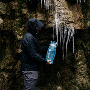 Person füllt die Alpin Loacker Trinkblase für Sommer + Winter mit Schmelzwasser aus eisbedecktem Felsen, ideal für Outdoor-Aktivitäten wie Wandern und Trekking.