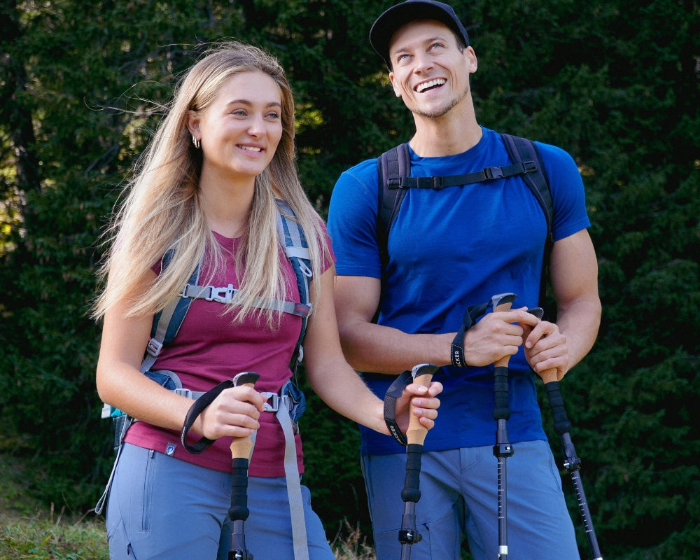 Ein Mann und eine Frau mit Wanderstöcken, beide tragen Outdoor-Kleidung und Rucksäcke, im Freien lächelnd, passend für Outdoor-Aktivitäten von alpinloacker.com.