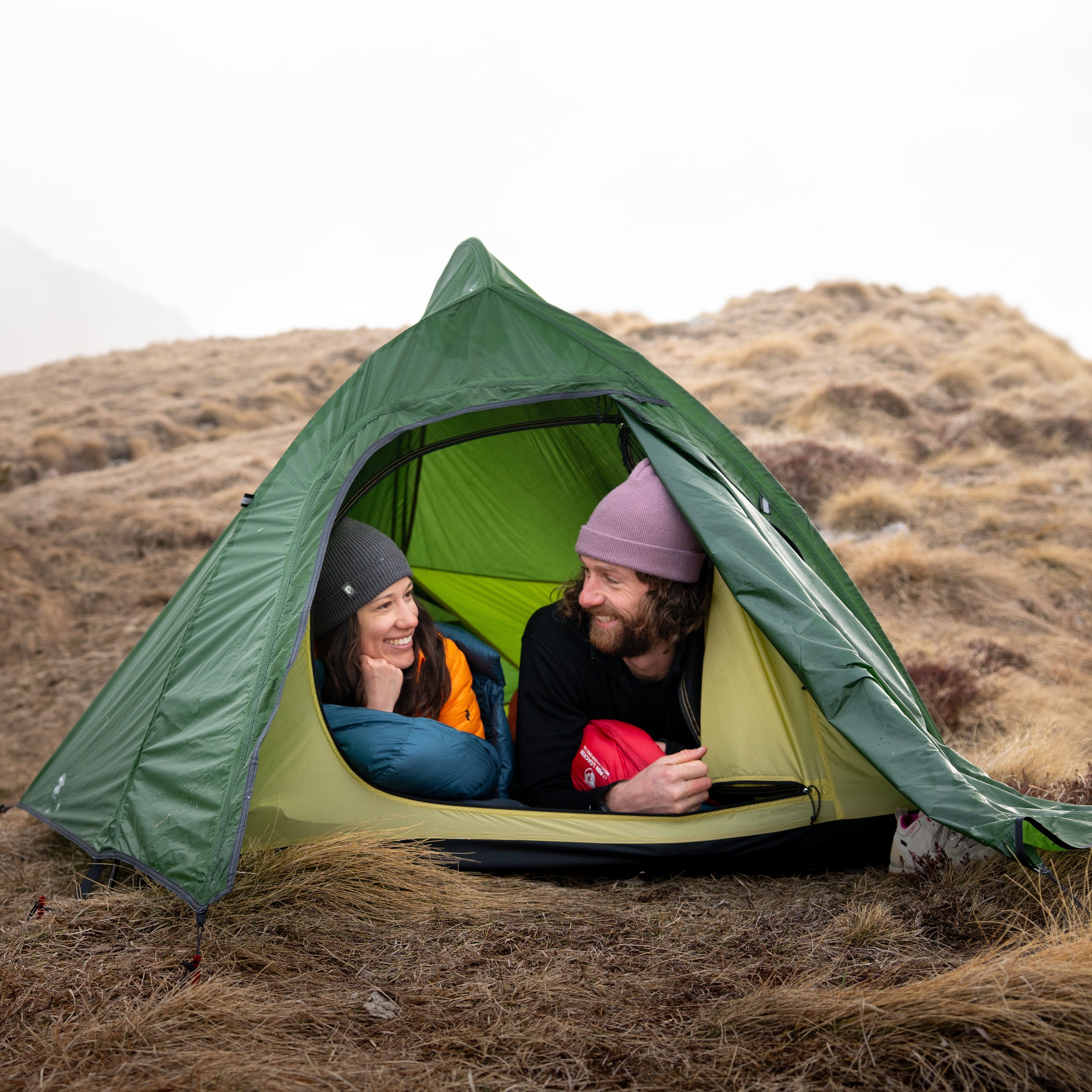 Eine Frau kniet in einem Zelt, umgeben von Pflanzen, passend zur Outdoor-Ausrüstung von Alpinloacker für Camping und Wandern.