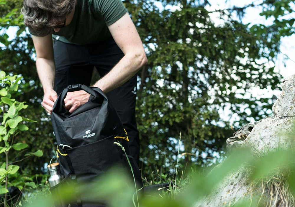 Ein Mann betrachtet einen Rucksack im Freien, passend für Outdoor-Aktivitäten wie Wandern, im Einklang mit Alpinloacker's Sortiment.
