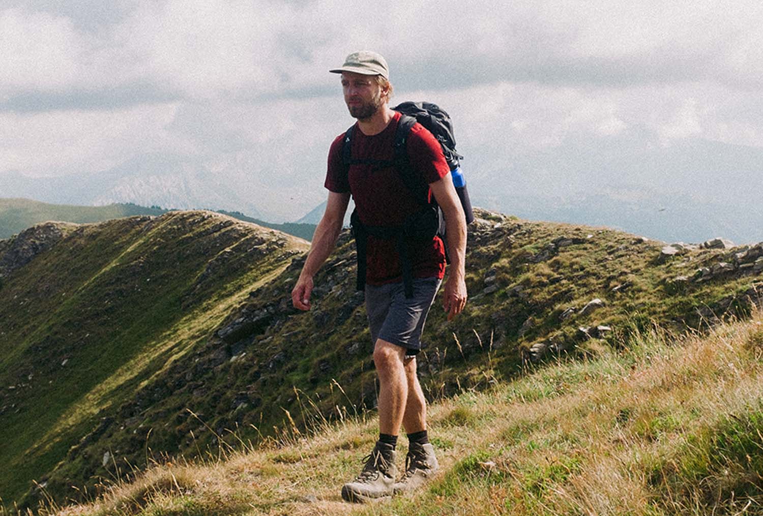 Ein Mann wandert mit Rucksack auf einem Berg, umgeben von Himmel und Wolken, repräsentiert Outdoor-Abenteuer und Ausrüstung von alpinloacker.com.