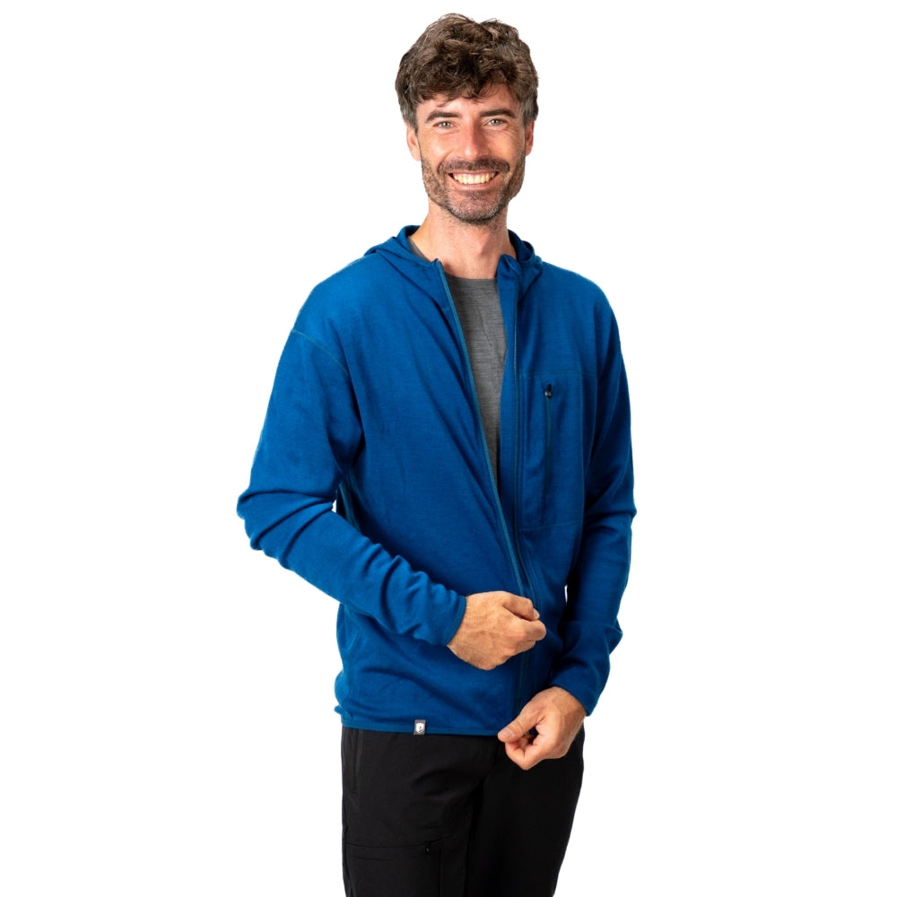 Mann mit blauem 100% Merino Sport Hoody Zip Herren - 230 g/m², lächelt, hält Reißverschluss. Ideal für Outdoor-Aktivitäten, atmungsaktiv und temperaturregulierend.
