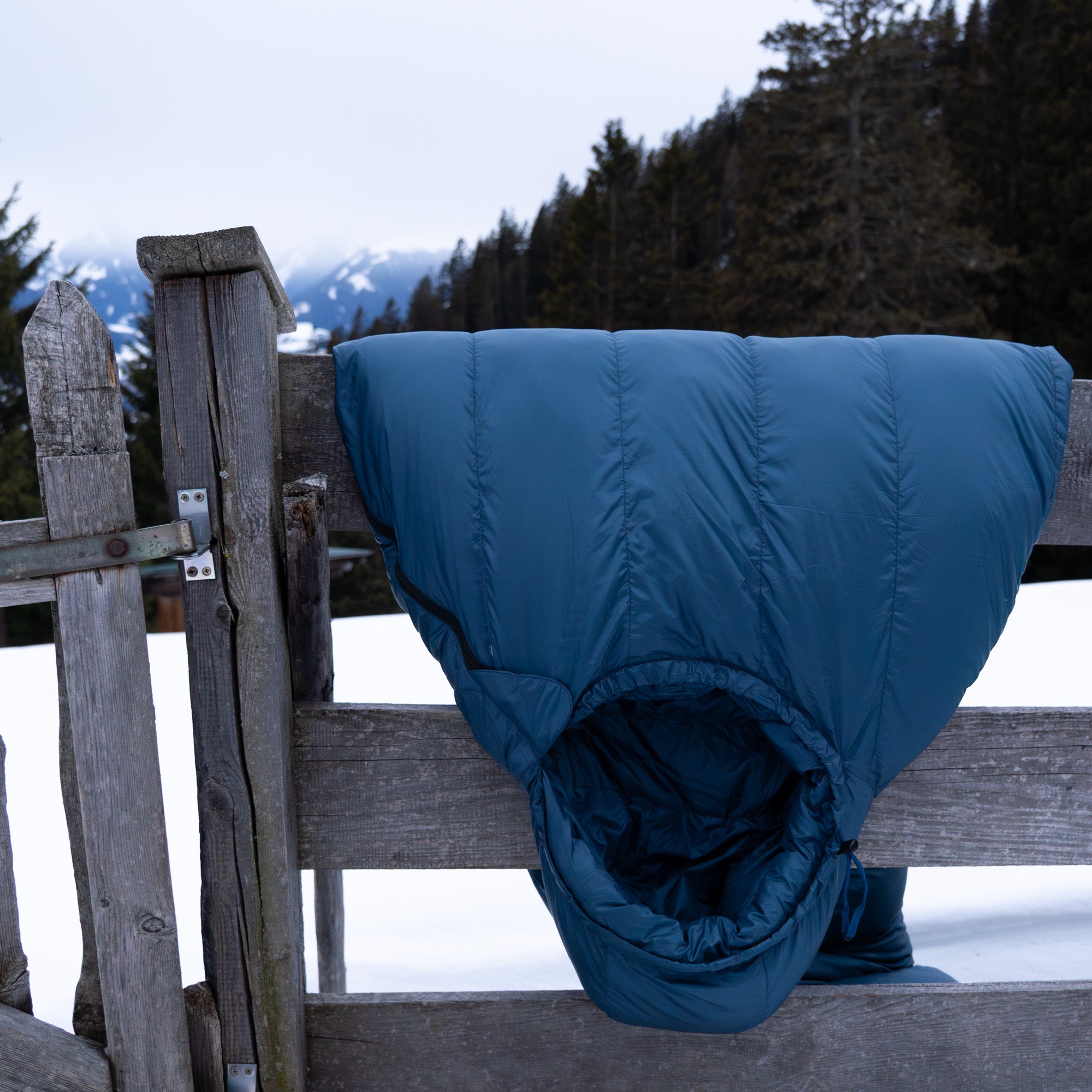 Down Pro 3 + Schlafsack von Alpin Loacker hängt über einem Zaun in Winterlandschaft, perfekt für Temperaturen bis knap unter 0°C. 