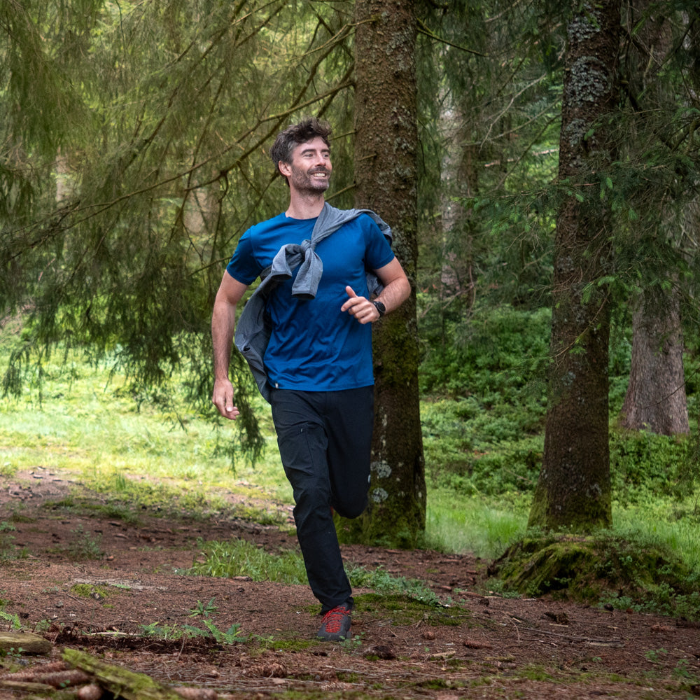 Mann joggt im Wald, trägt das 100% Merino T-Shirt Herren 160 g/m² - ultrafein, ideal für Outdoor-Aktivitäten, kombiniert Komfort und Leistung, passend zum Outdoor-Shop-Konzept.