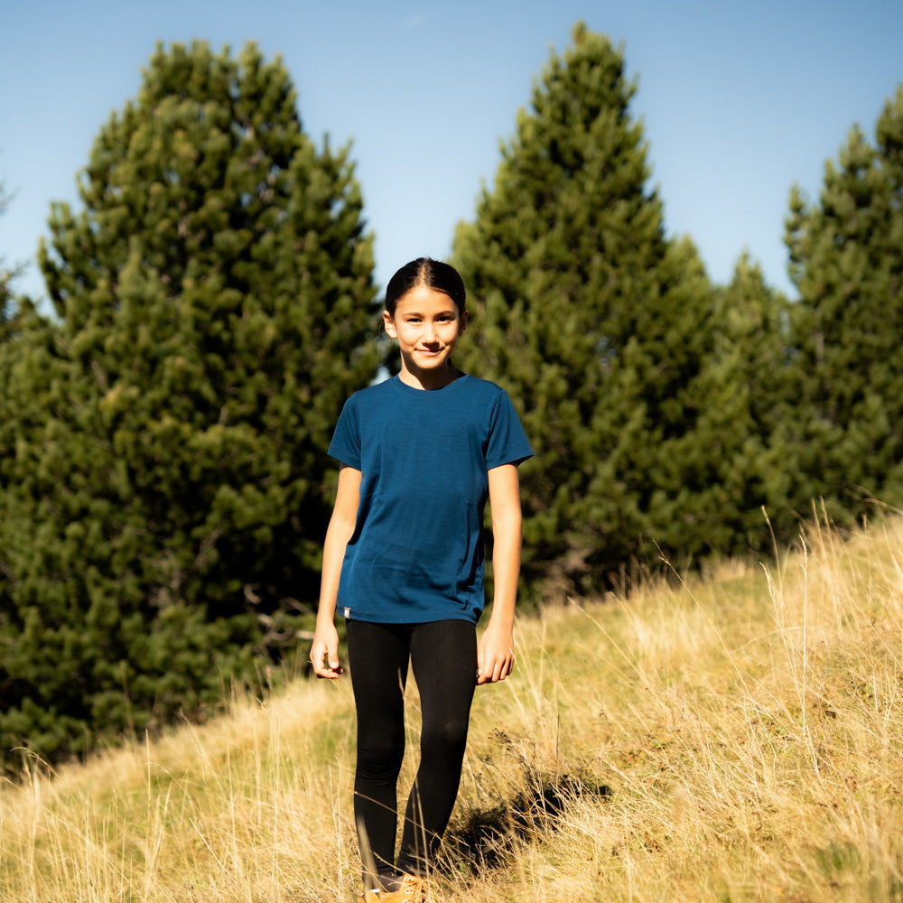 Ein junges Mädchen trägt das Kinder Merino T Shirt 150g/m2, ideal für Outdoor-Abenteuer, mit Komfort und Strapazierfähigkeit durch CoreSpoon-Merinowolle.