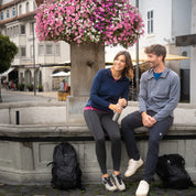 Paar mit Alpin Loacker 100% Merinowolle Jacke Herren 160 g/m², sitzt an einem Brunnen. Jacken zeigen Outdoor-Funktionalität und Komfort.