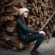 Ein Mädchen sitzt in 100% Merino langarm Set in grün vor einem Holzstapel