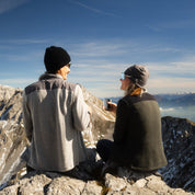Wanderpärchen sitzt auf dem Gipfel mit 230g/m2 Merino Mützen in grau und schwarz