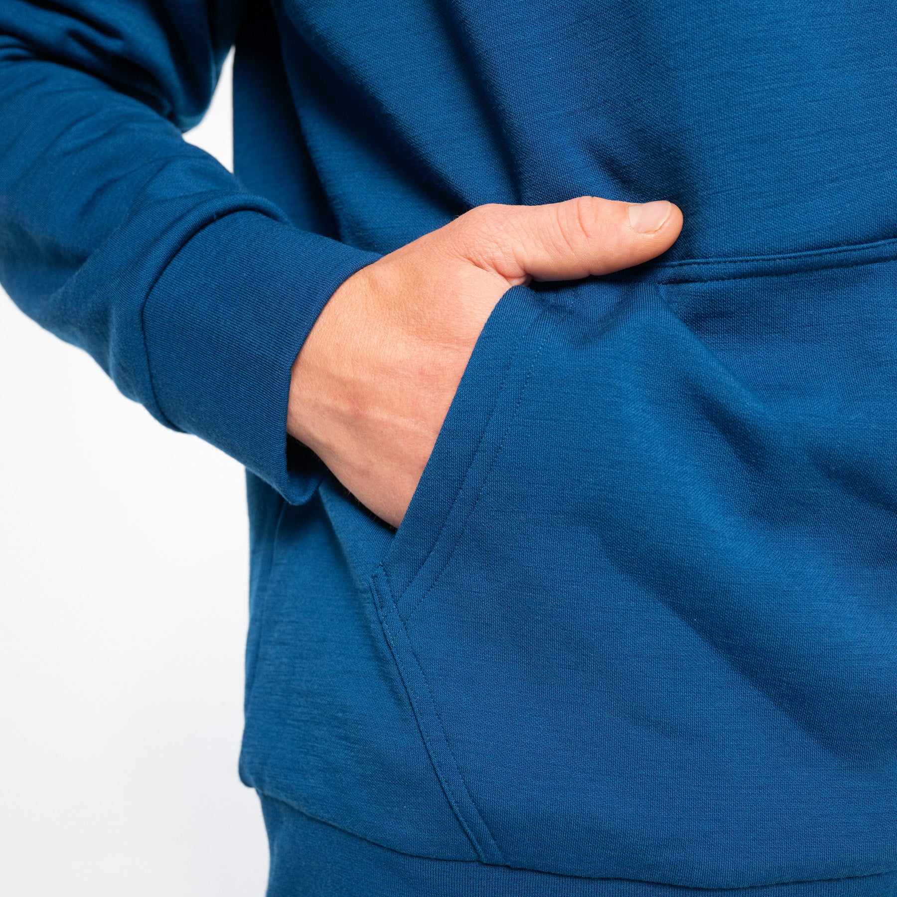 Model trägt blauen Alpin Loacker Merino Hoodie. Close-up auf die Bauchtasche