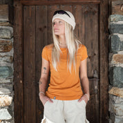 Model steht in orange farbenem Corespun Merino T-Shirt vor einer Holztür