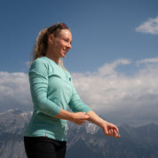 Model steht vor Bergkulisse und richtet sich den Ärmel des Coolmax Longsleeve Shirts von Alpin Loacker