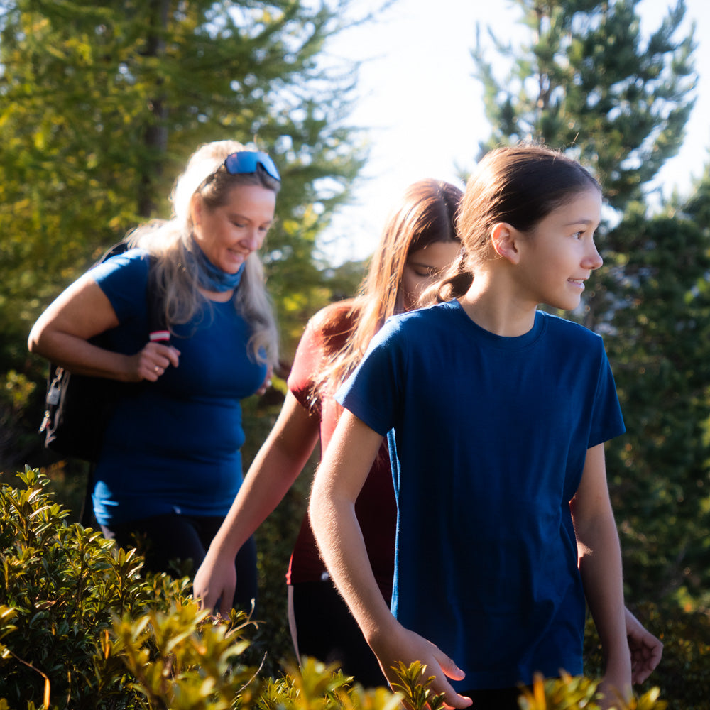 Eine Familie läuft durch die Natur, die Kinder tragen Merino T-Shirts von Alpin Loacker in blau und rot