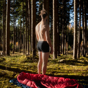 Model steh in schwarzer Merino Coolmax Boxer im Wald neben seinem Camp Spot