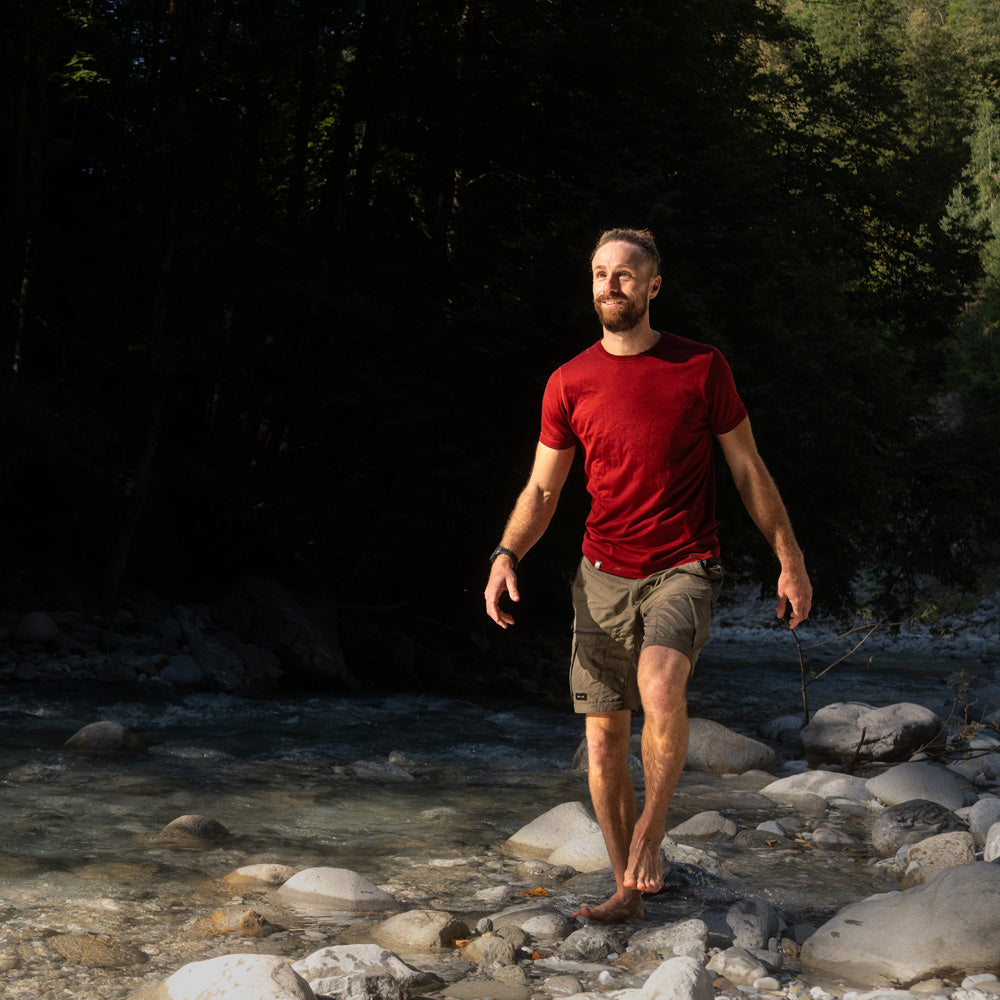 Mann läuft durch Flußbett und trägt rotes 180g Merino Shirt - perfekt für alle Outdoor Aktivitäten