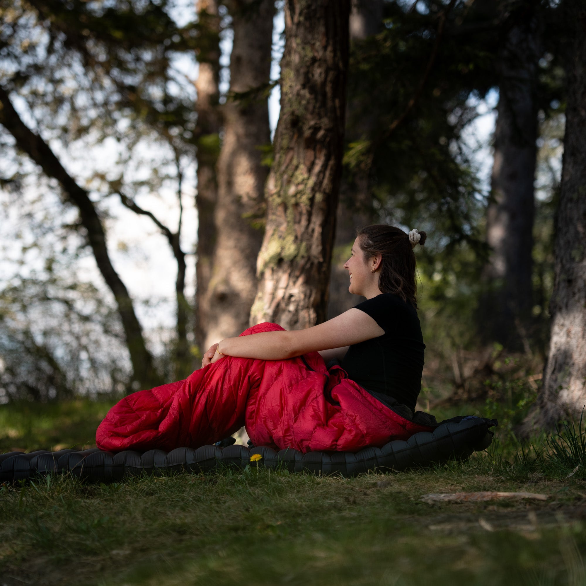 Model sitzt in rotem Sommerdaunenschlafsack im Wald