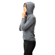 Frau im Profil mit grauer 100% Merinowolle Jacke Damen 160 g/m² - ultrafein, Kapuze aufgesetzt, kombiniert mit schwarzen Leggings, ideal für Outdoor-Abenteuer.