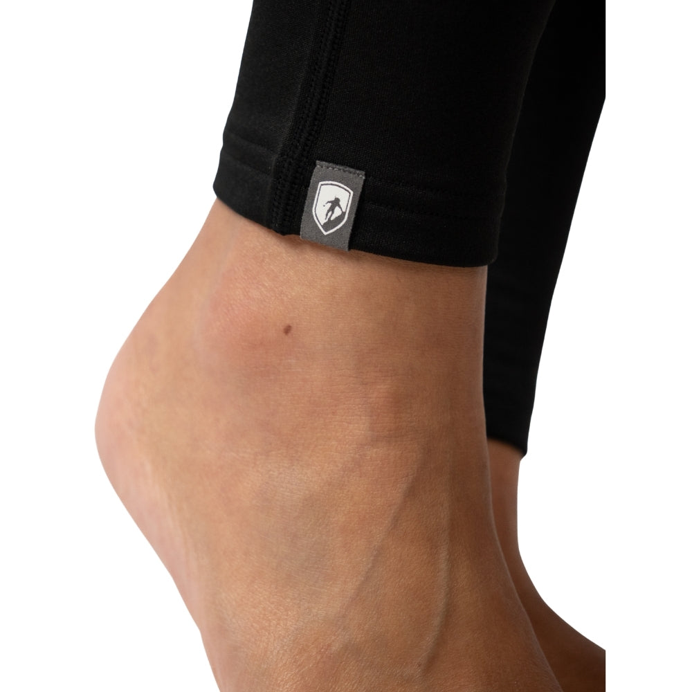 Nahaufnahme eines nackten Knöchels in schwarzen Merino Leggings/Hose Damen - 290 g/m2 mit grauem Logo-Etikett am Saum, ideal für Yoga und unterwegs.