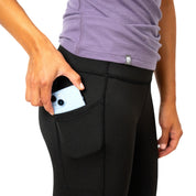 Person steckt ein Smartphone in die Seitentasche der Merino Leggings/Hose Damen - 290 g/m2, hoch tailliert und ideal für Bewegung und Reisen.