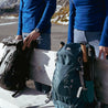 Ein Paar auf einer Bank mit Rucksäcken und einem Fokus auf faltbare Wanderstöcke aus Carbon, ideal für Outdoor-Aktivitäten.