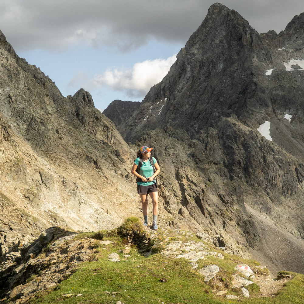 Frau steht mit Coolmax Merino T-Shirt in Mineral Farbe auf dem Berg und schließt ihren Hüftgurt vom Rucksack