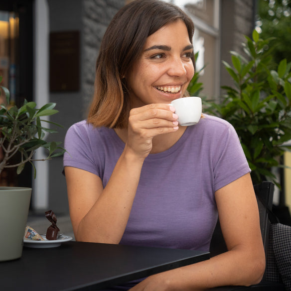 Junge Frau im Freien mit Merino T-Shirt Damen 150g/m2, genießt Kaffee. Ideal für Outdoor-Aktivitäten, vereint Komfort und Strapazierfähigkeit durch Corespun Merinowolle.
