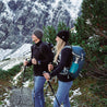 Couple hiking with Merino jacket men 270 g/m², equipped with trekking poles and backpacks, through snowy mountain landscape. Ideal for outdoor adventures.