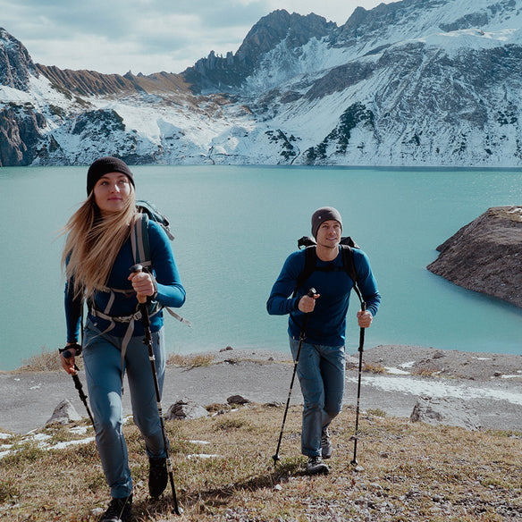 Merino Langarm Shirt Damen 230 g/m2: Mann und Frau wandern mit Stöcken, tragen funktionales Merino-Langarmshirt für Komfort und Temperaturregulierung bei Outdoor-Aktivitäten.