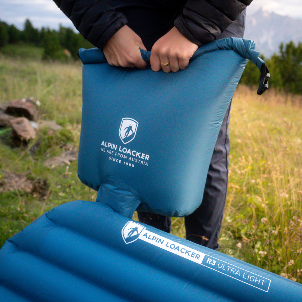 Frau pumpt blaue Isomatte auf Wiese mit Pumpsack auf
