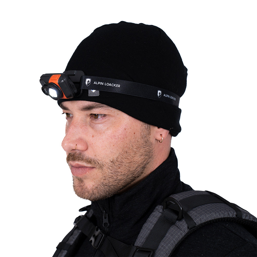 L'homme au chapeau noir porte une lampe frontale LED légère, 700 lumens, idéale pour les aventures en plein air comme le camping et la randonnée, avec un bandeau réglable et une grande puissance d'éclairage.