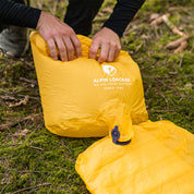 Hände öffnen eine gelbe Tasche der ultraleichten Isomatte, isoliert mit Kunstdaune, ideal für Outdoor-Abenteuer.