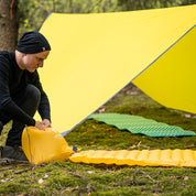 Mann platziert eine gelbe Ultraleichte Isomatte isoliert mit Kunstdaune auf dem Boden neben einem gelben Zelt, ideal für Outdoor-Abenteuer.