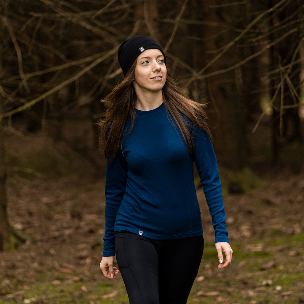 Frau beim Wandern im Wald trägt das Merino Langarmshirt Damen 150 g/m², ideal für Outdoor-Aktivitäten, mit CORESPUN-Technologie und atmungsaktiver Merinowolle.