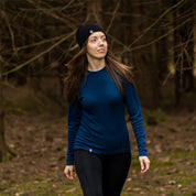 Frau beim Wandern im Wald trägt das Merino Langarmshirt Damen 150 g/m², ideal für Outdoor-Aktivitäten, mit CORESPUN-Technologie und atmungsaktiver Merinowolle.