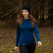 Frau trägt Merino Langarmshirt Damen 150 g/m² im Wald, ideal für Outdoor-Aktivitäten dank temperaturregulierender, geruchsneutraler Merinowolle, geeignet für Wandern und Alltag.